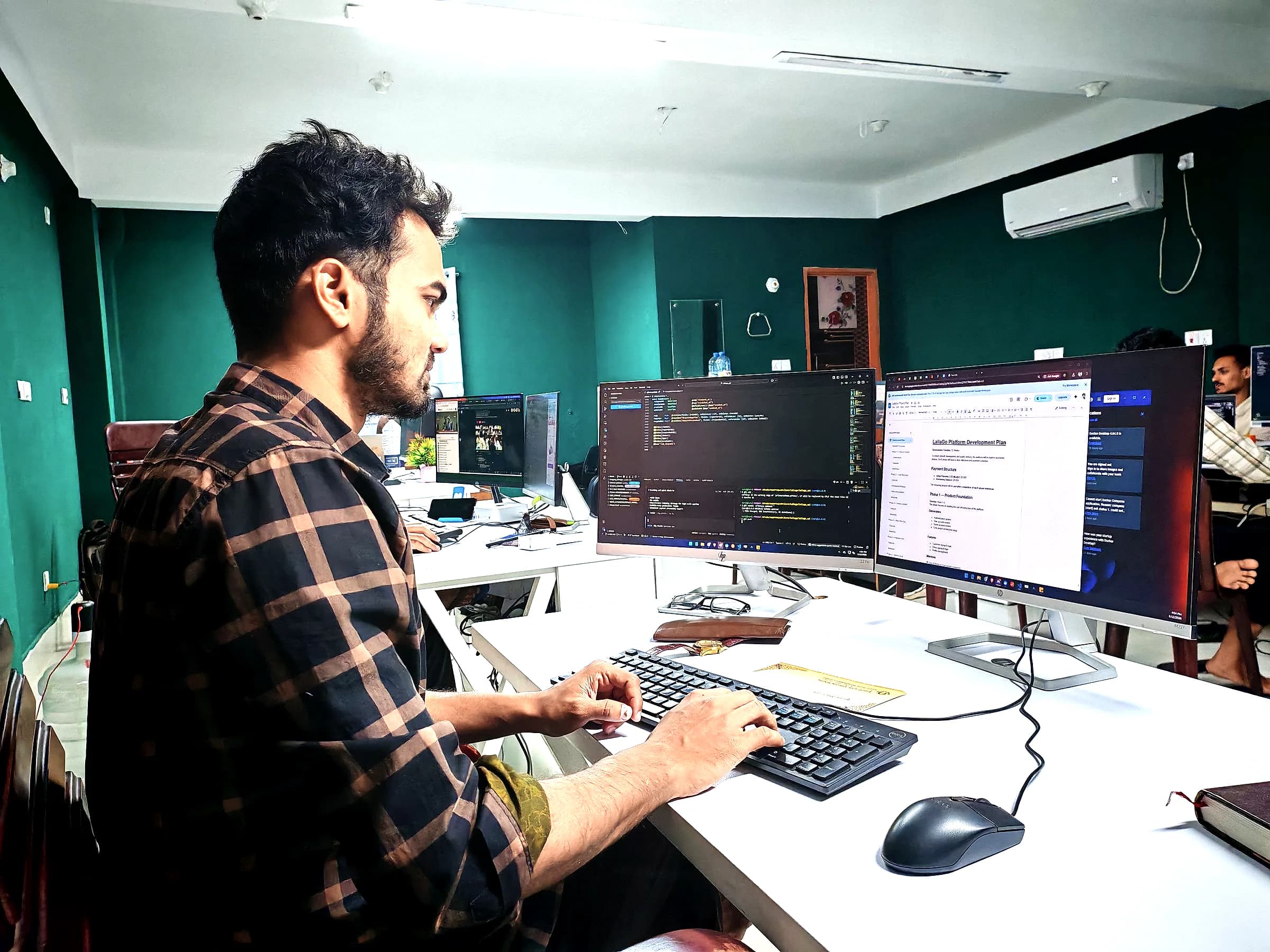 A developer works at two monitors of code in a green-walled office