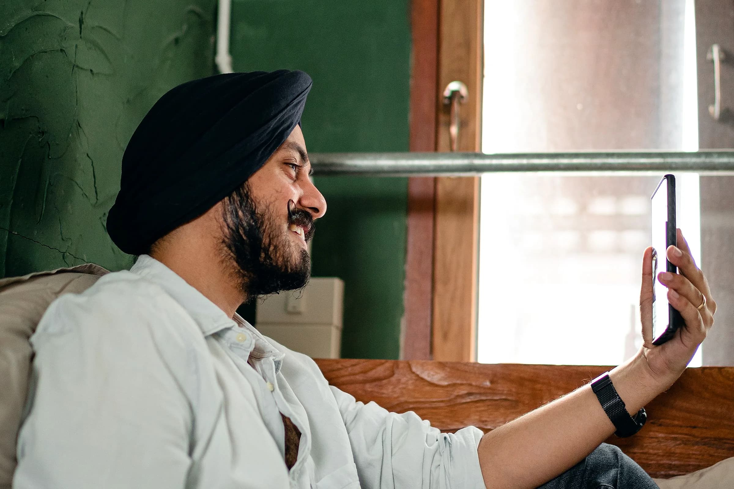 A young man in a turban smiles at his phone on a video call